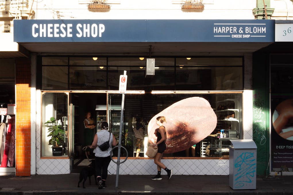 The outside of a store with the sun shining and people walking past.